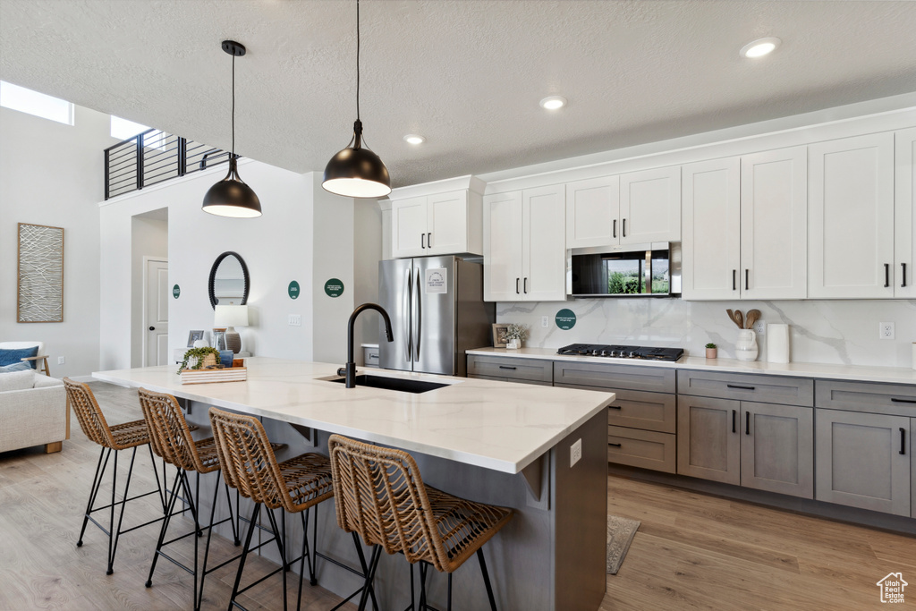 Kitchen featuring appliances with stainless steel finishes, a kitchen bar, tasteful backsplash, a kitchen island with sink, and light stone counters