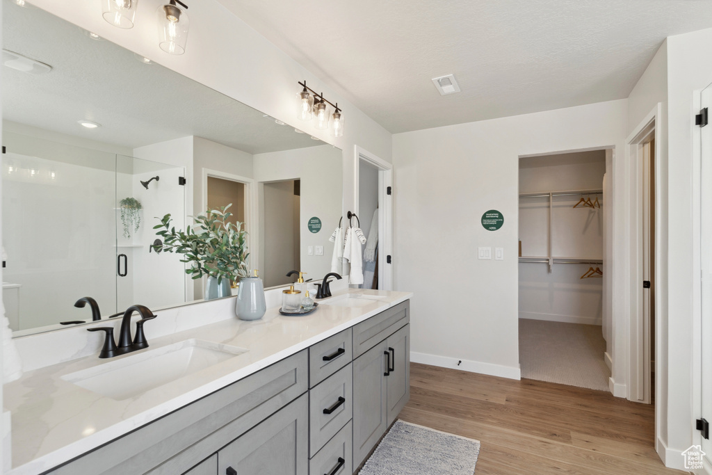 Bathroom featuring double vanity, a shower stall, wood finished floors, and a walk in closet
