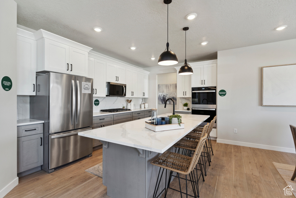 Kitchen with appliances with stainless steel finishes, a breakfast bar, light wood-style flooring, white cabinetry, and recessed lighting