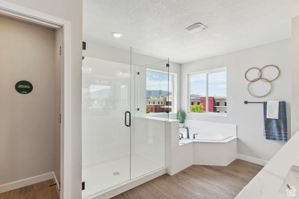 Full bath with wood finished floors, a stall shower, a garden tub, a textured ceiling, and vanity