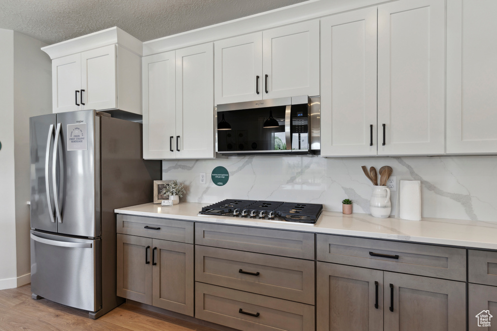 Kitchen featuring appliances with stainless steel finishes, light wood-style flooring, decorative backsplash, white cabinetry, and gray cabinets