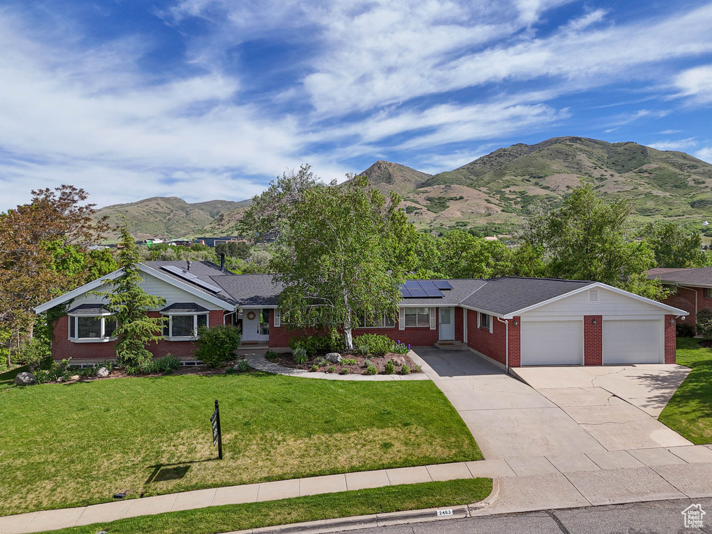 Ranch-style house featuring brick siding, roof mounted solar panels, a mountain view, driveway, and a front lawn