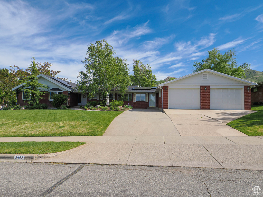 Single story home featuring a front yard, brick siding, roof mounted solar panels, concrete driveway, and an attached garage