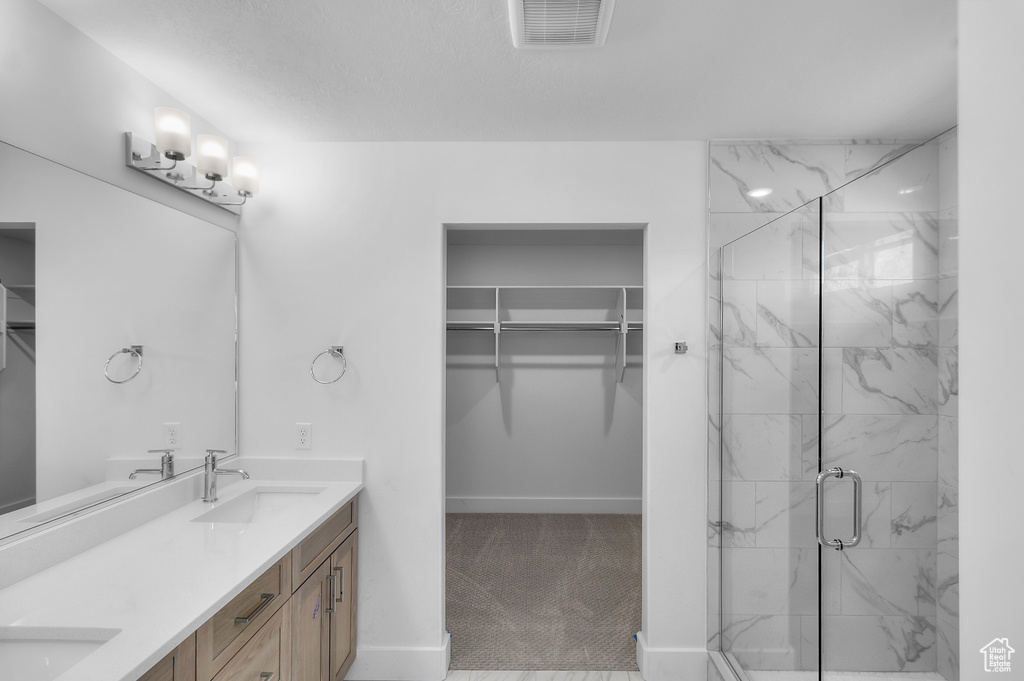 Bathroom with a spacious closet, double vanity, a sink, visible vents, and a marble finish shower