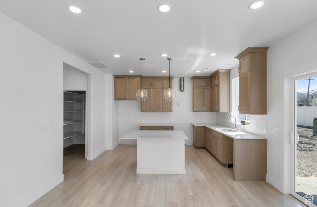 Kitchen with recessed lighting, light wood-style flooring, a kitchen island, backsplash, and a sink