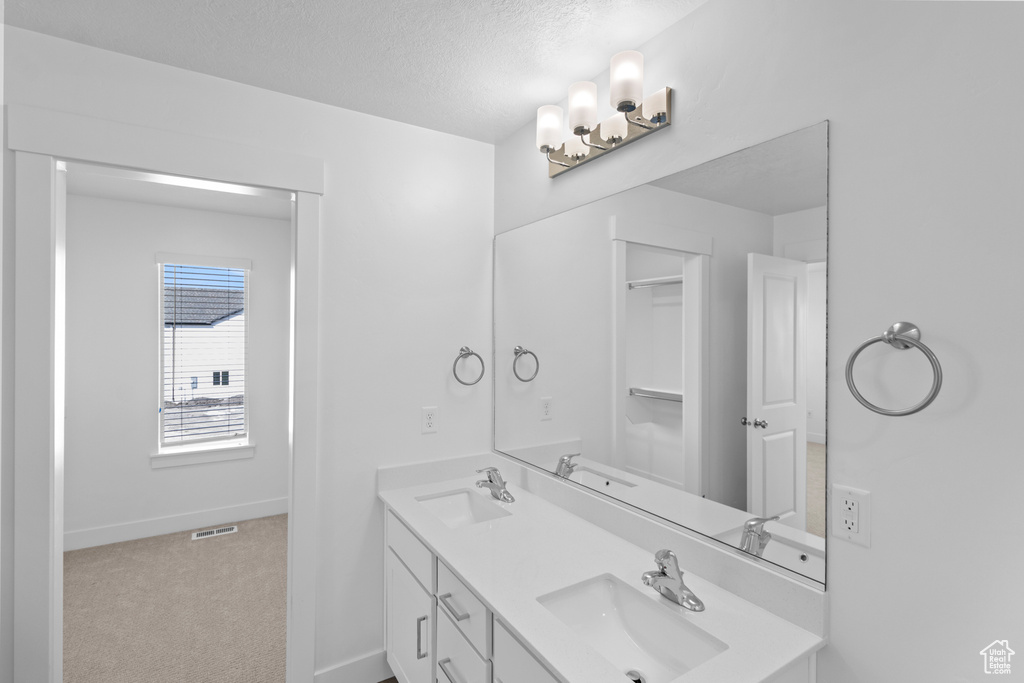 Bathroom with baseboards, a textured ceiling, double vanity, and a sink