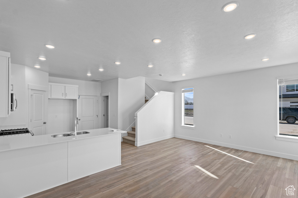 Unfurnished living room featuring recessed lighting, stairway, a sink, baseboards, and light wood-type flooring