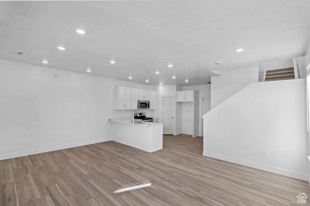 Unfurnished living room featuring recessed lighting, stairs, light wood finished floors, and baseboards