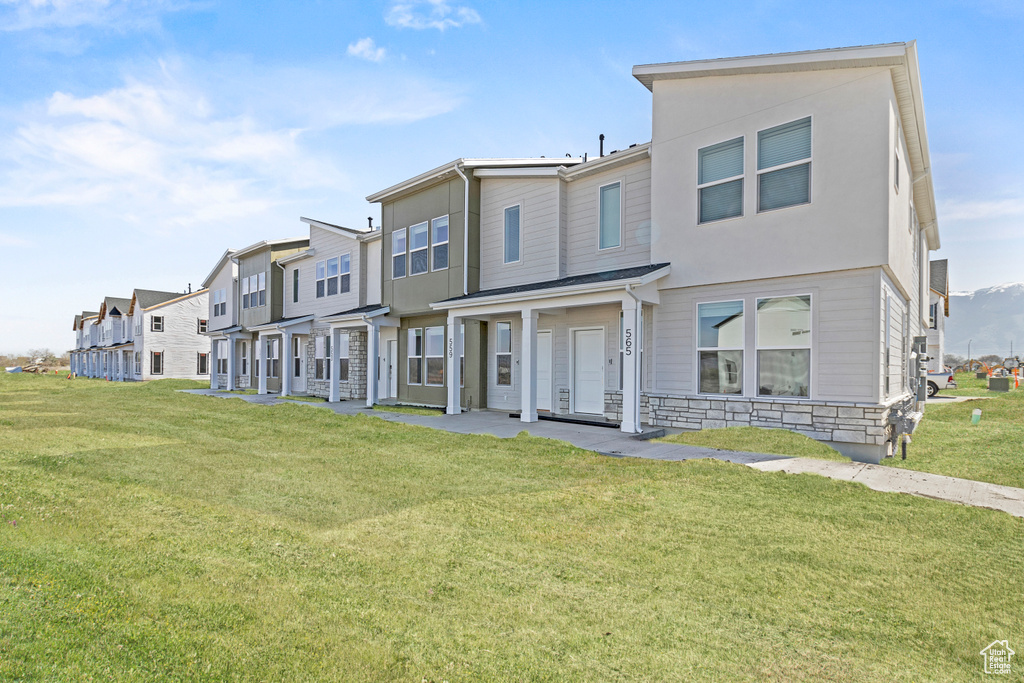 Townhome / multi-family property featuring a residential view, a front lawn, and stone siding