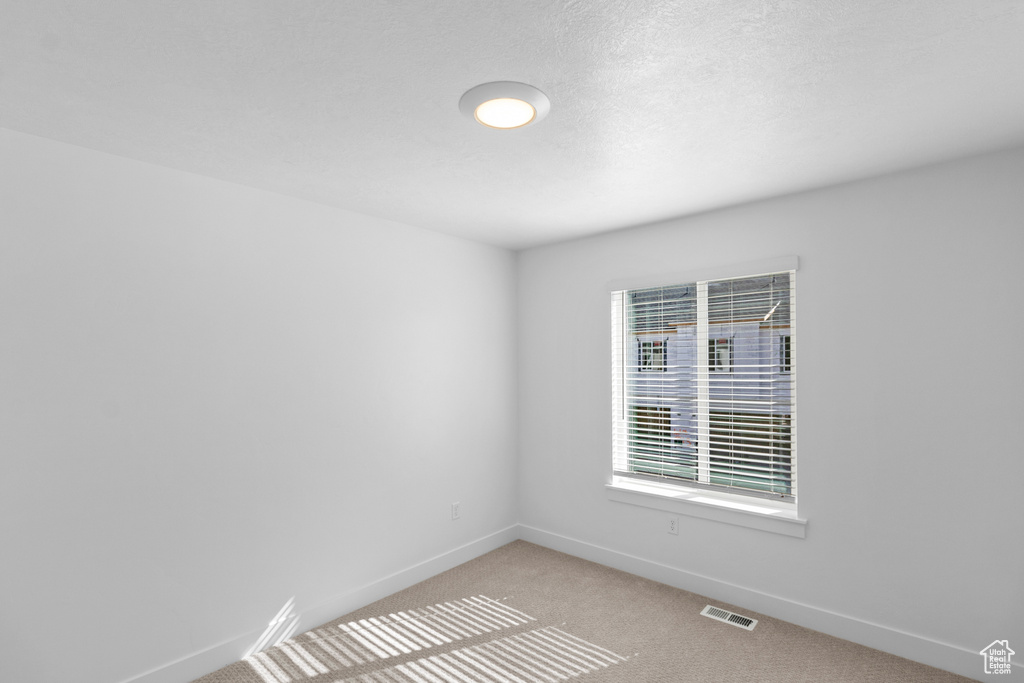 Spare room featuring visible vents, light carpet, and baseboards