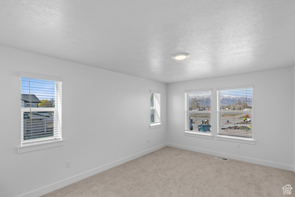 Spare room with a textured ceiling, visible vents, light carpet, and baseboards