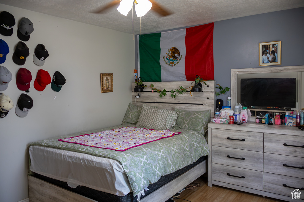 Bedroom with a textured ceiling, wood finished floors, and a ceiling fan