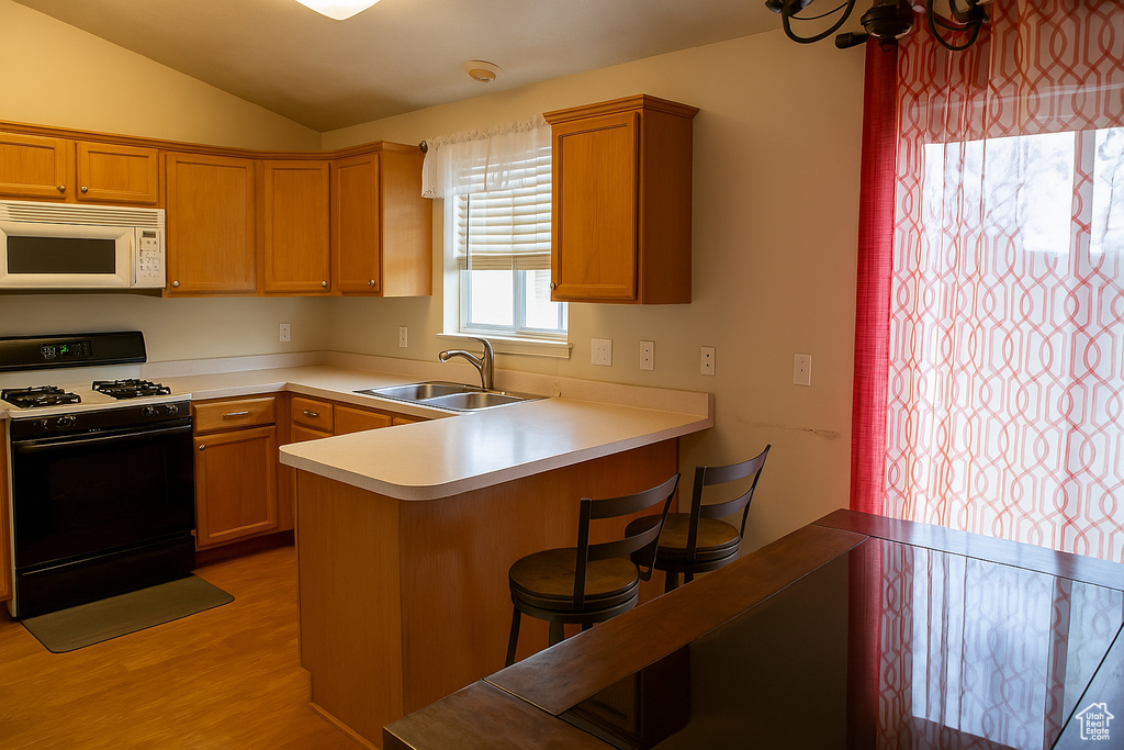 Kitchen with white microwave, vaulted ceiling, gas stove, a sink, and light wood finished floors