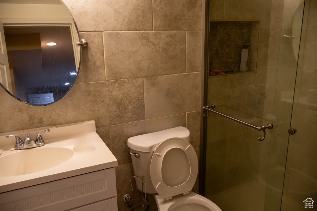 Full bath featuring toilet, a stall shower, vanity, and tile walls