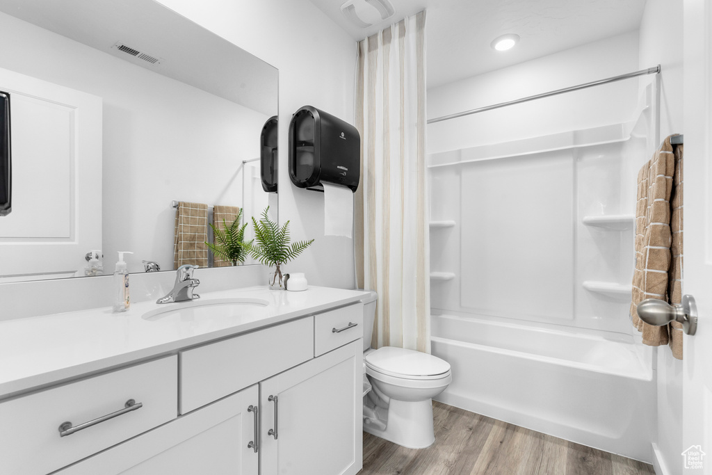 Bathroom with visible vents, shower / bath combination with curtain, toilet, vanity, and wood finished floors