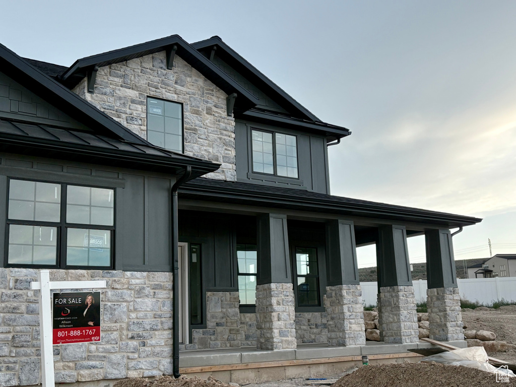 View of front of house featuring stone siding, board and batten siding, a standing seam roof, covered porch, and metal roof
