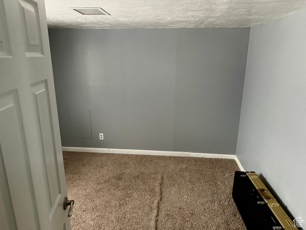 Carpeted spare room featuring a textured ceiling and baseboards
