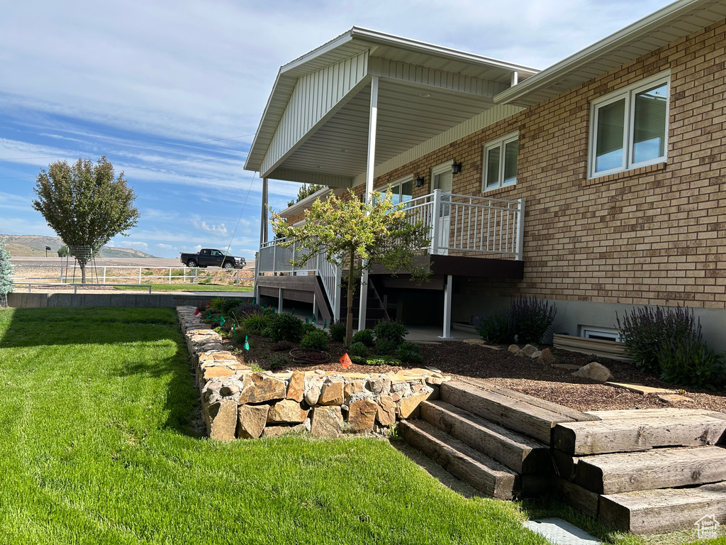 View of property exterior featuring brick siding, a lawn, a deck, and stairs