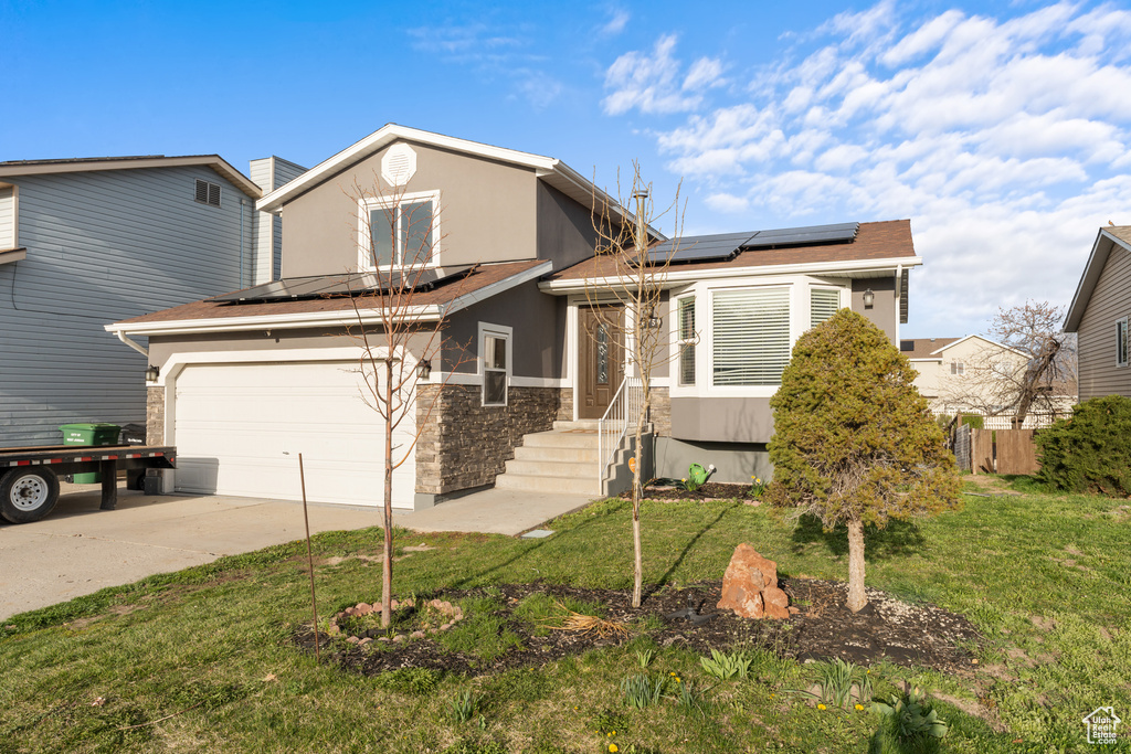 View of front of home featuring solar panels, stone siding, stucco siding, a front lawn, and driveway