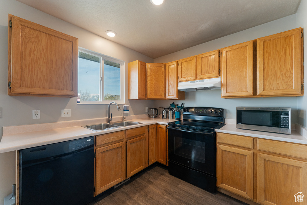 Kitchen featuring dark wood-style flooring, light countertops, black appliances, under cabinet range hood, and a sink