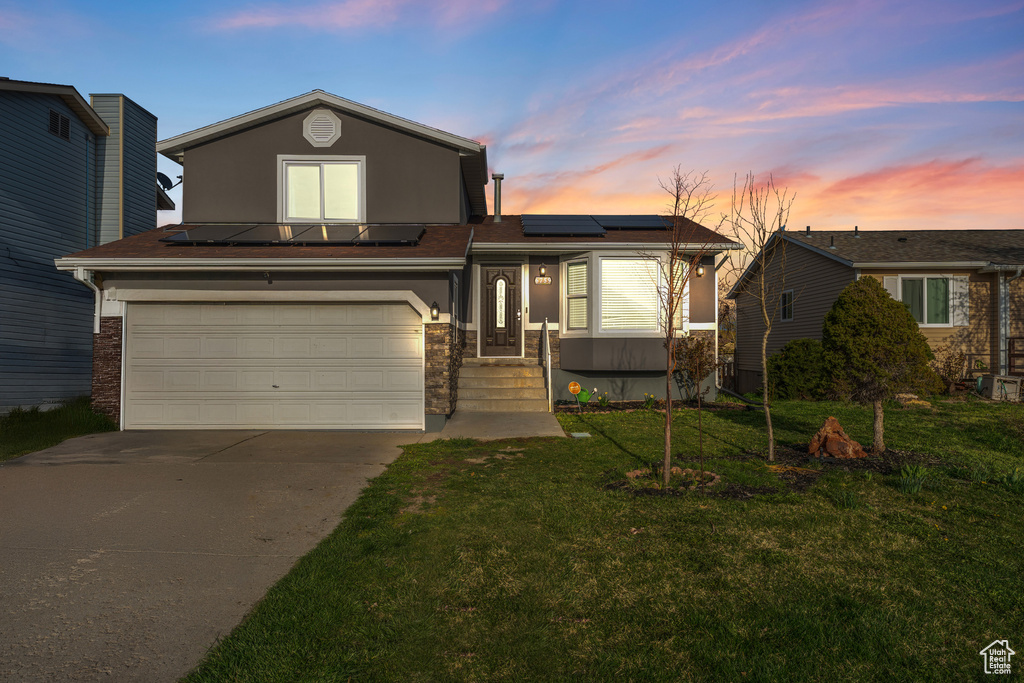View of front of house featuring a garage, driveway, a front lawn, and roof mounted solar panels