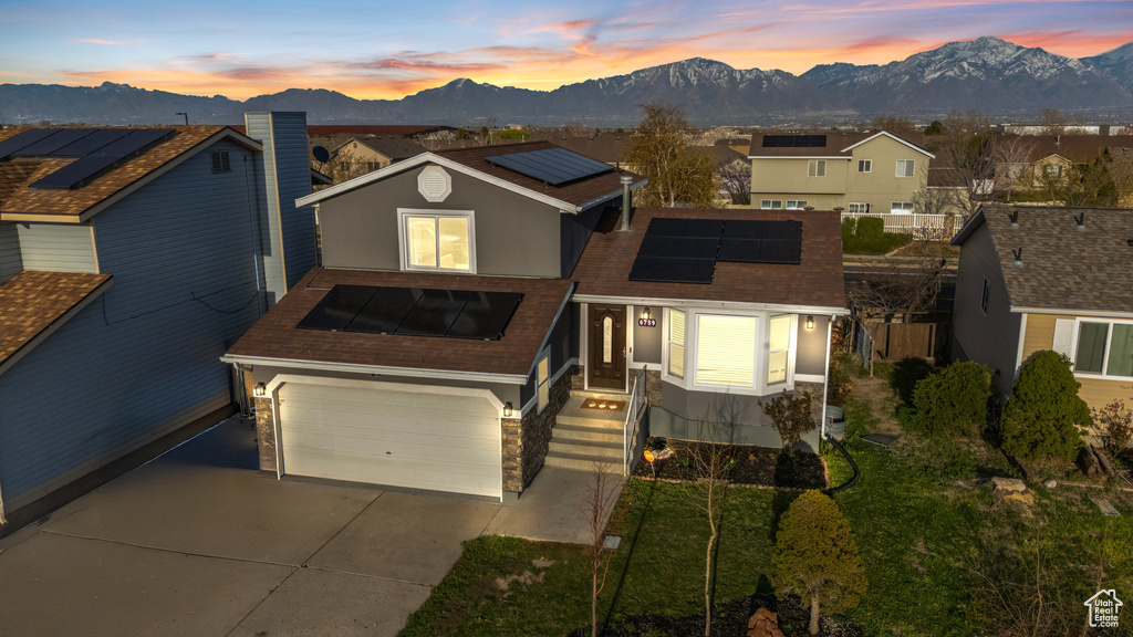 View of front of house featuring a garage, concrete driveway, solar panels, a mountain view, and a residential view