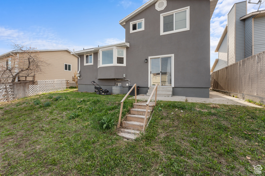 Back of property with entry steps, stucco siding, fence, and a lawn