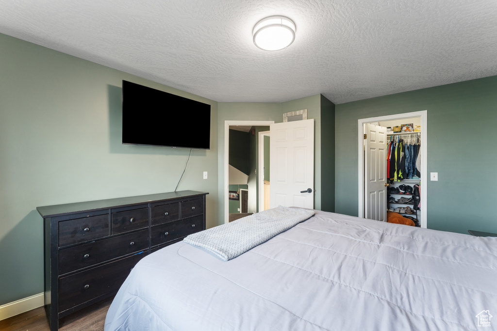 Bedroom featuring a closet, baseboards, dark wood-style floors, a textured ceiling, and a walk in closet