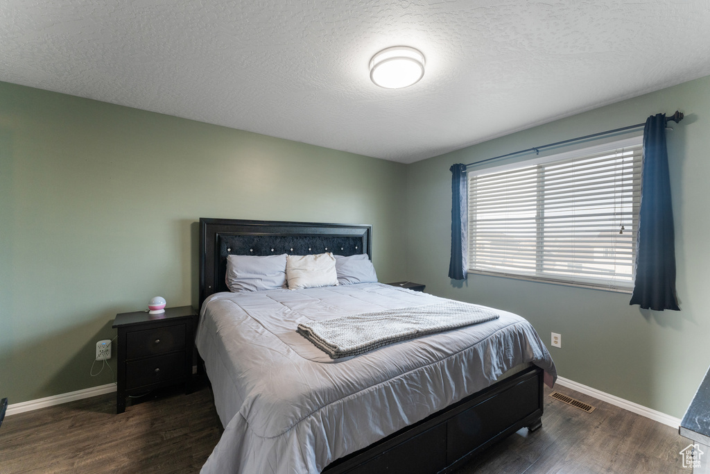 Bedroom featuring visible vents, baseboards, a textured ceiling, and wood finished floors