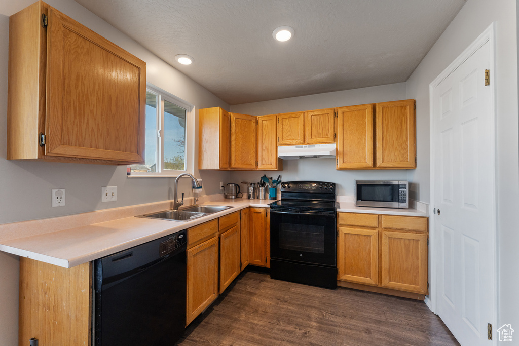 Kitchen with a sink, black appliances, dark wood-style floors, and under cabinet range hood