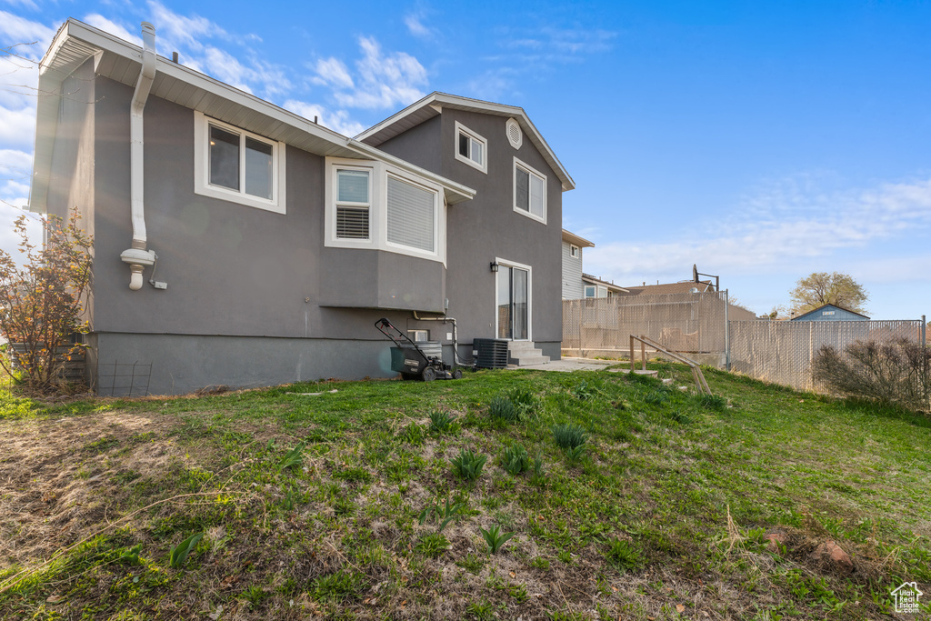 Rear view of house featuring central air condition unit, a yard, stucco siding, entry steps, and fence