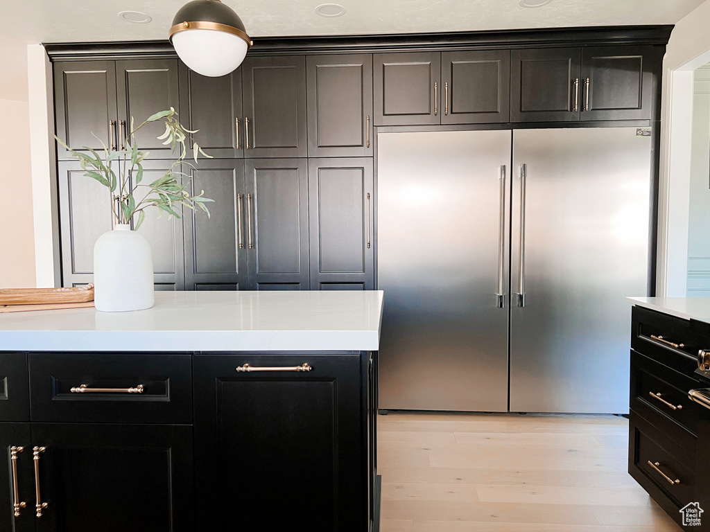 Kitchen with built in refrigerator, light countertops, light wood-style floors, and dark cabinets