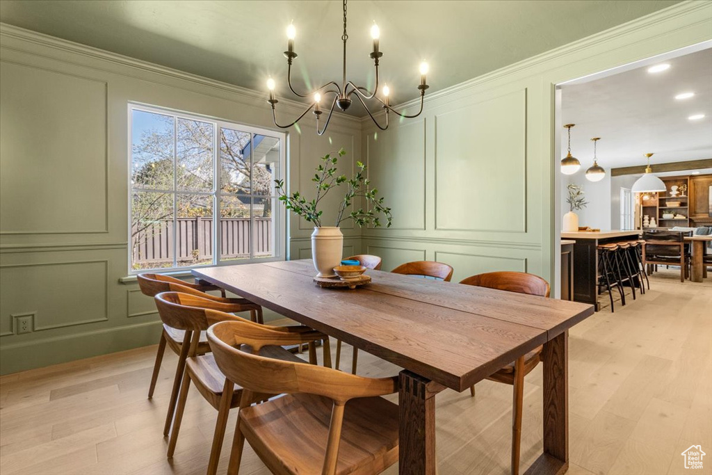 Dining area featuring crown molding, a decorative wall, recessed lighting, light wood finished floors, and a notable chandelier