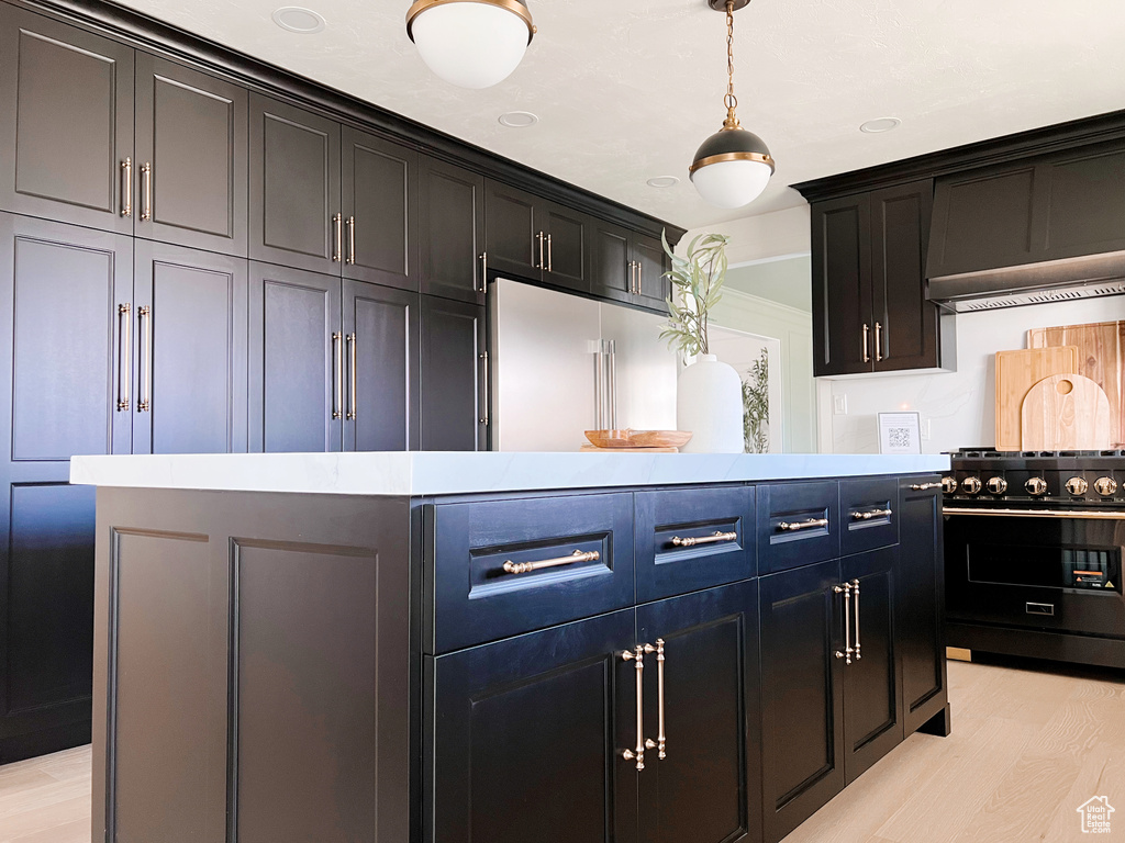 Kitchen featuring built in refrigerator, light wood-style flooring, light countertops, decorative light fixtures, and black gas stove