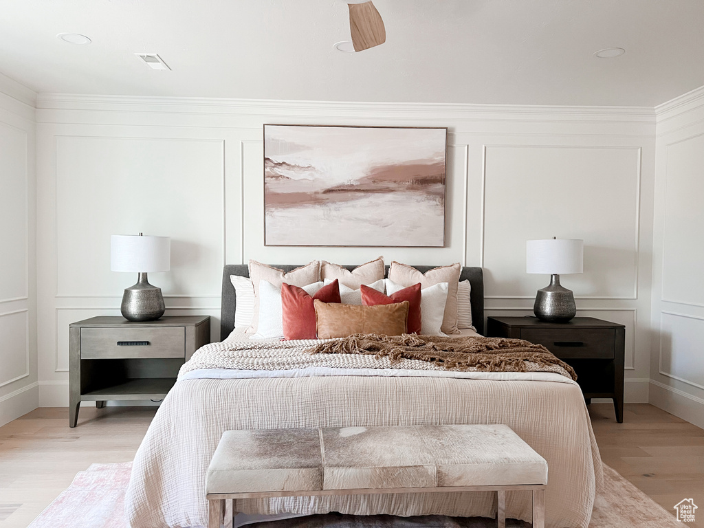 Bedroom with visible vents, a decorative wall, ornamental molding, ceiling fan, and light wood finished floors