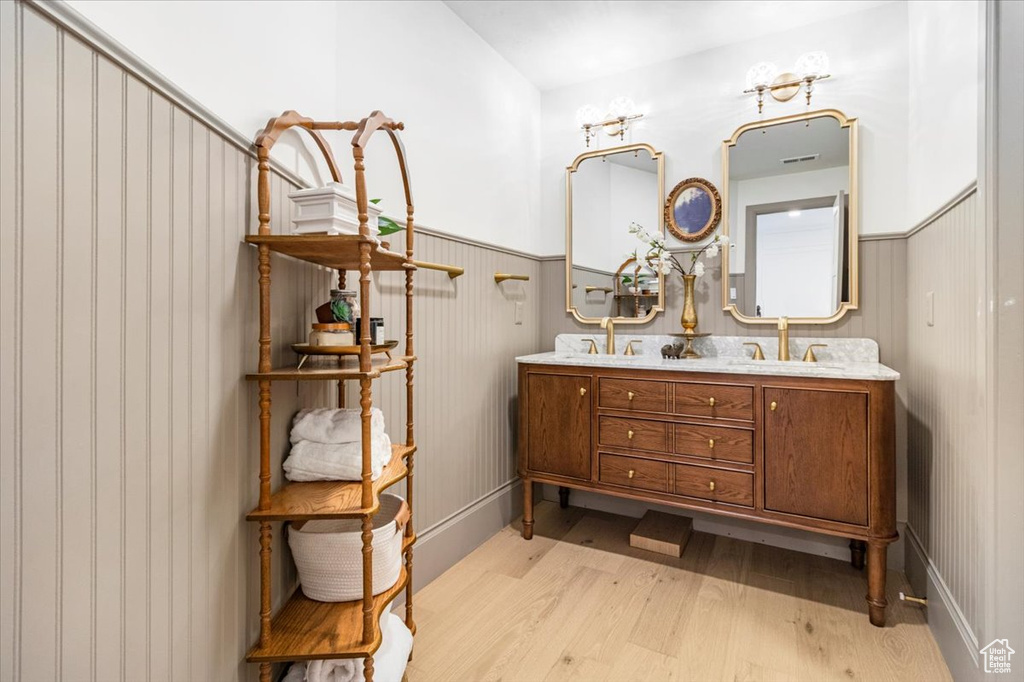 Full bath with a sink, a wainscoted wall, double vanity, and wood finished floors