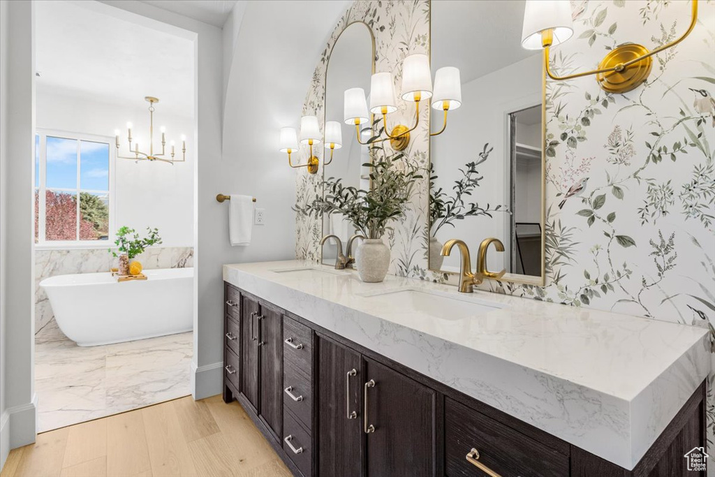 Full bathroom featuring double vanity, a notable chandelier, a sink, and a soaking tub