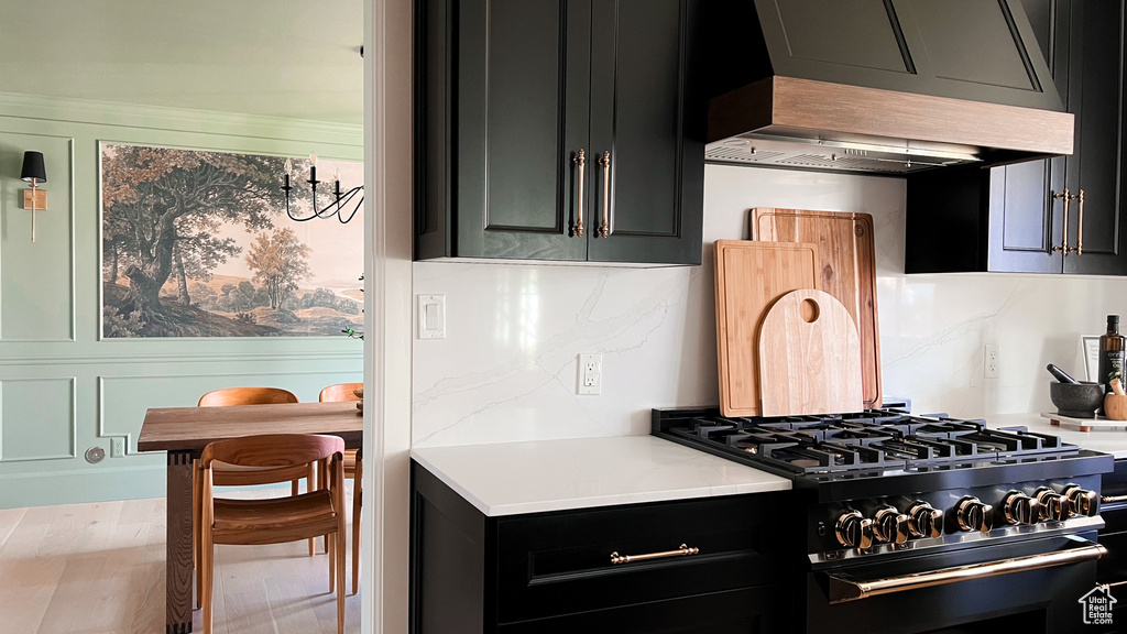 Kitchen featuring wall chimney range hood, light countertops, dark cabinetry, and gas range
