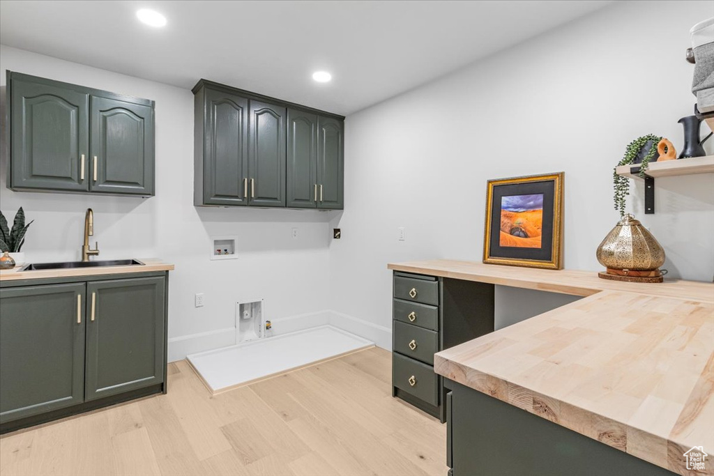 Laundry area with hookup for an electric dryer, washer hookup, cabinet space, light wood finished floors, and a sink