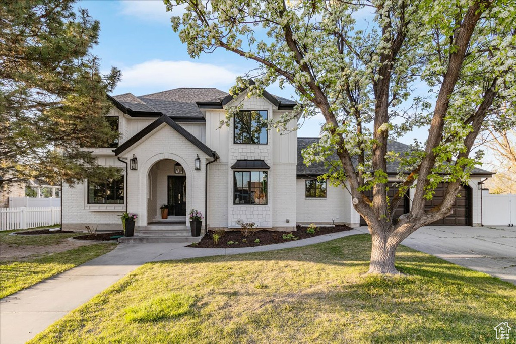 French country home with brick siding, a shingled roof, fence, and a front lawn