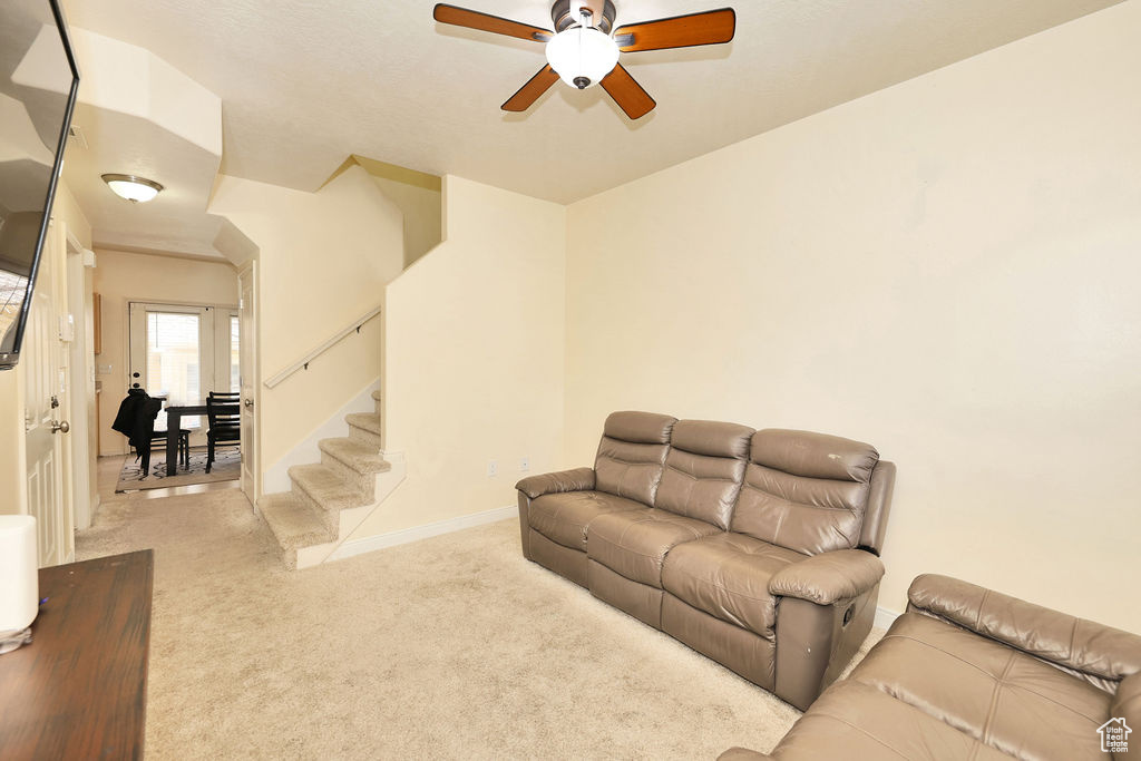 Living room featuring stairs, carpet flooring, baseboards, and a ceiling fan