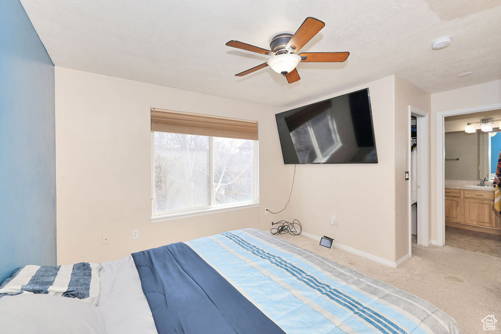 Bedroom with connected bathroom, a ceiling fan, light carpet, a sink, and baseboards
