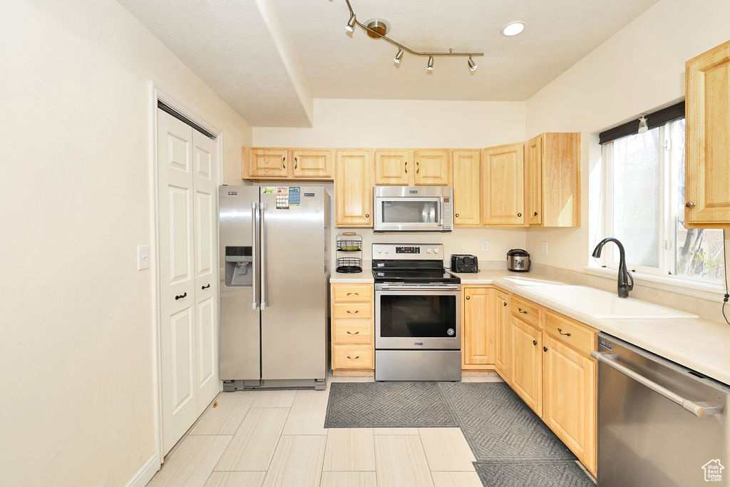 Kitchen featuring light countertops, a sink, light brown cabinetry, and appliances with stainless steel finishes