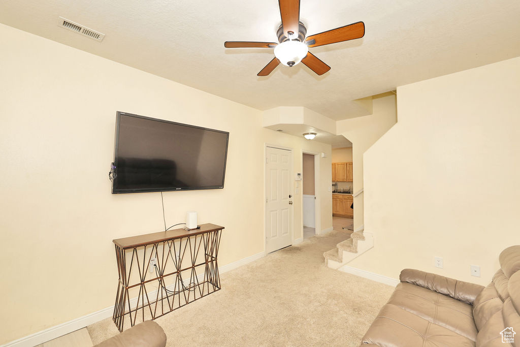 Living room featuring visible vents, baseboards, a ceiling fan, and light carpet