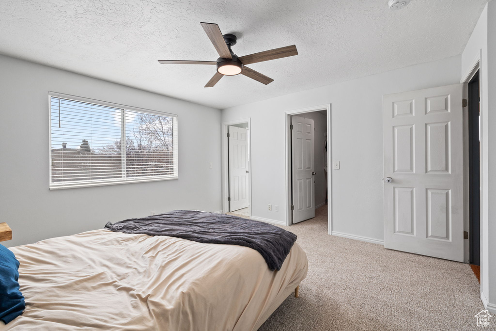 Bedroom with light carpet, a textured ceiling, baseboards, and a ceiling fan