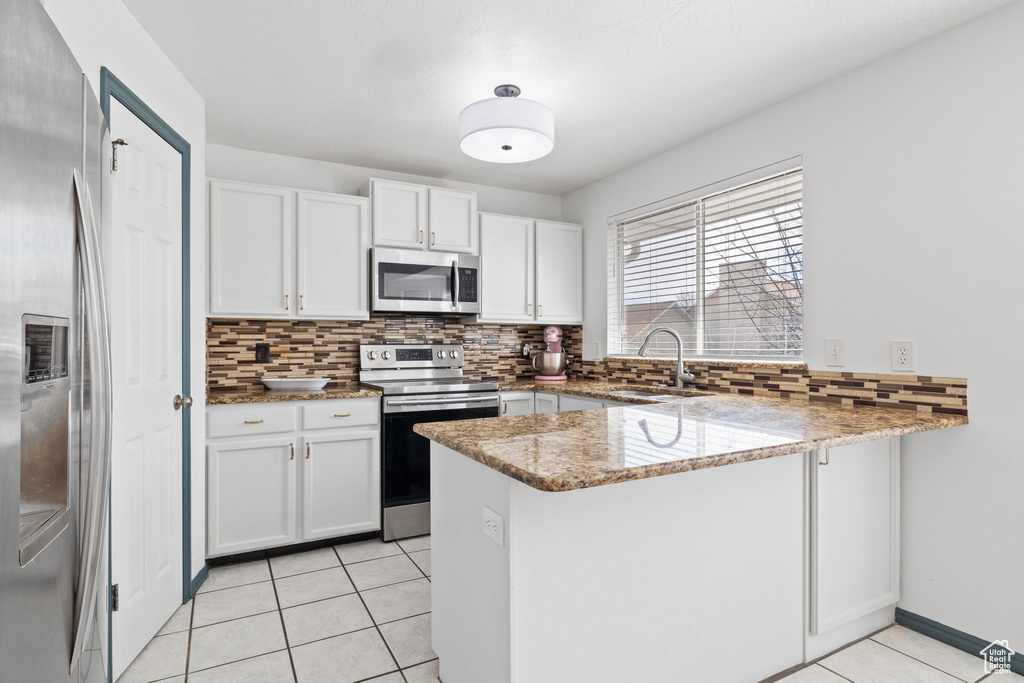 Kitchen featuring light tile patterned floors, a sink, appliances with stainless steel finishes, a peninsula, and decorative backsplash