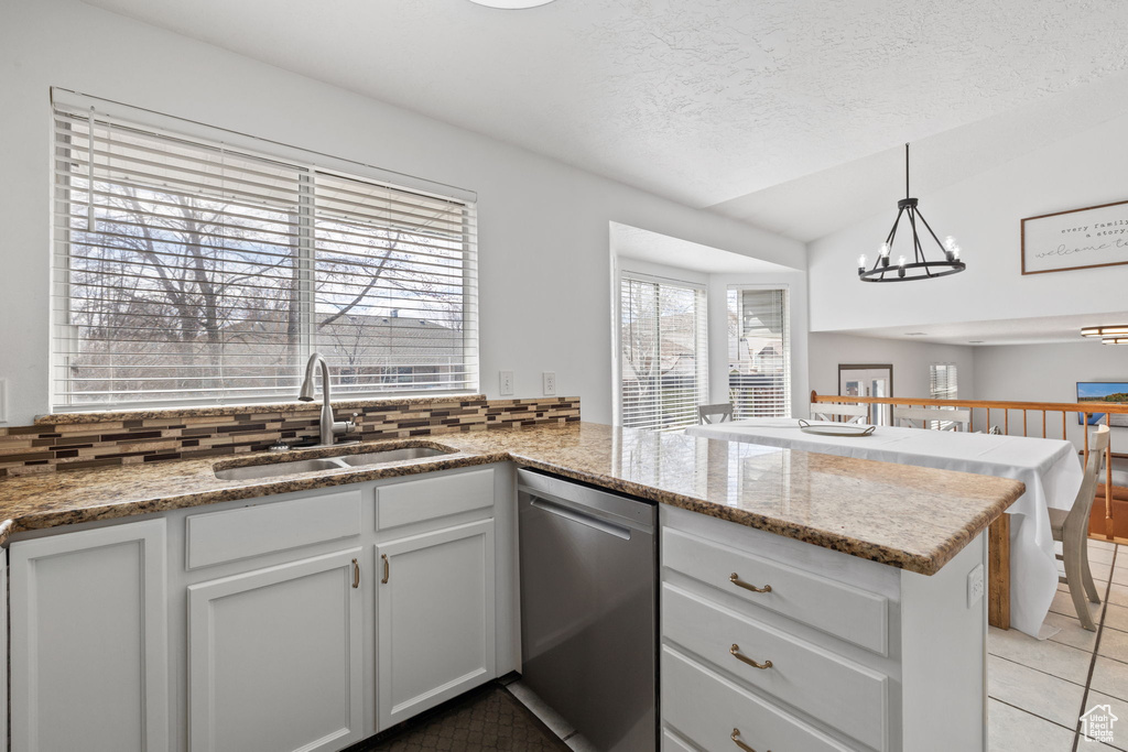 Kitchen with an inviting chandelier, a peninsula, light tile patterned floors, dishwasher, and a sink