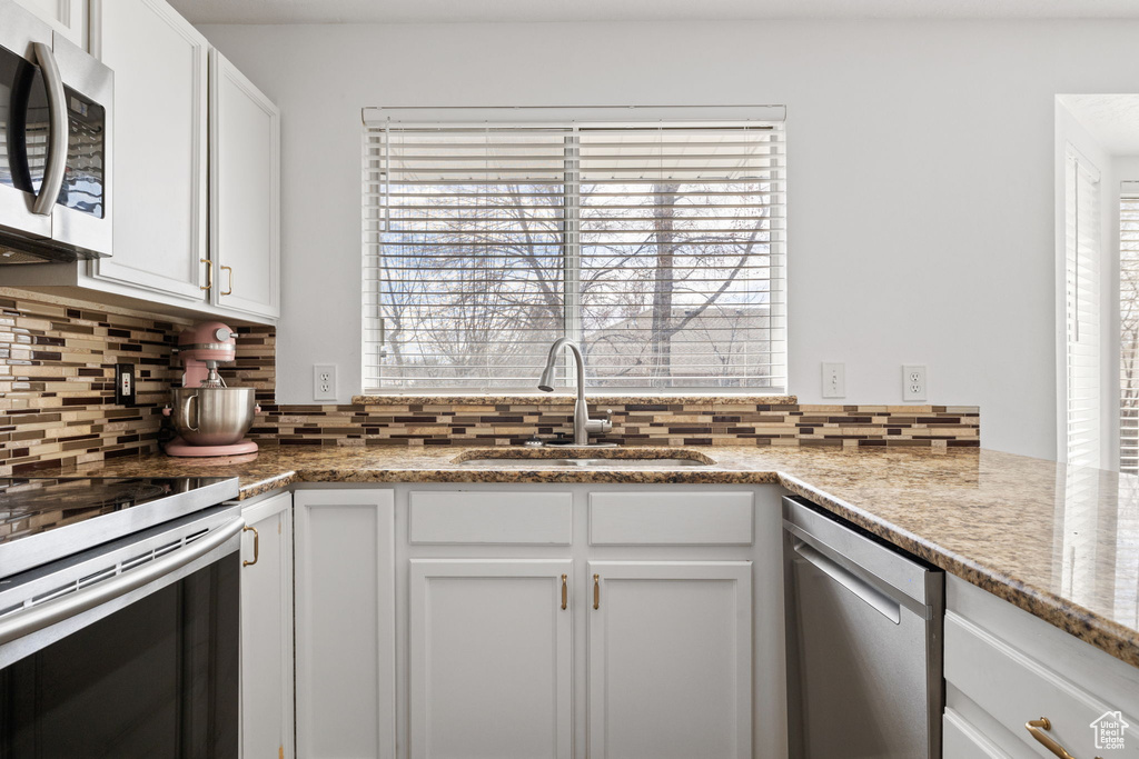 Kitchen with decorative backsplash, a sink, white cabinetry, and stainless steel appliances