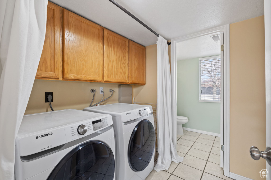 Laundry area featuring cabinet space, light tile patterned floors, washer and clothes dryer, and baseboards