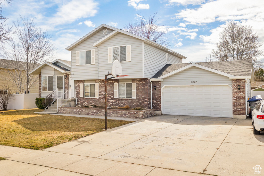 View of front of property with a front yard, fence, brick siding, a garage, and concrete driveway